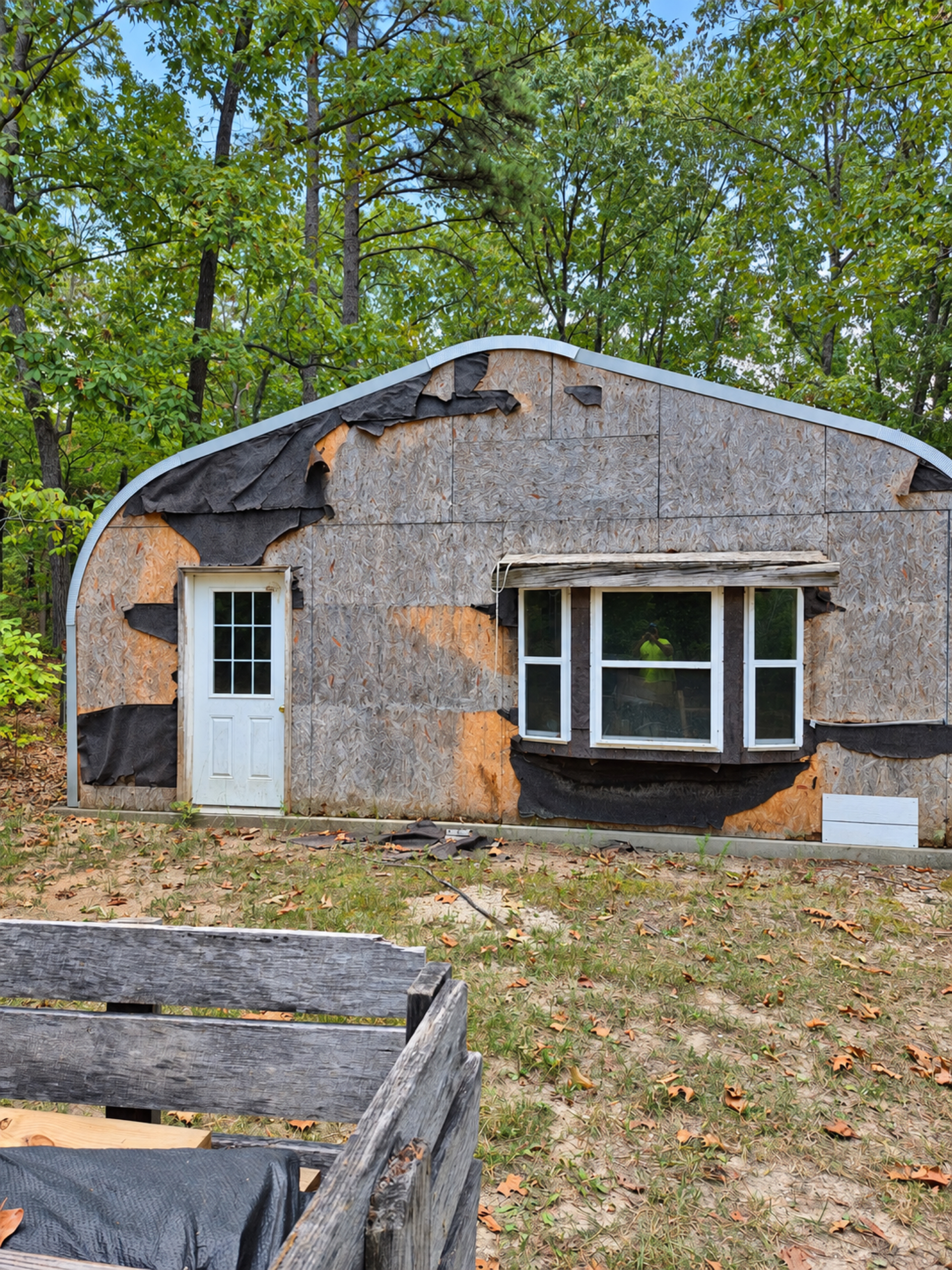 Garage end wall with exposed sheathing, a white entry door and three windows