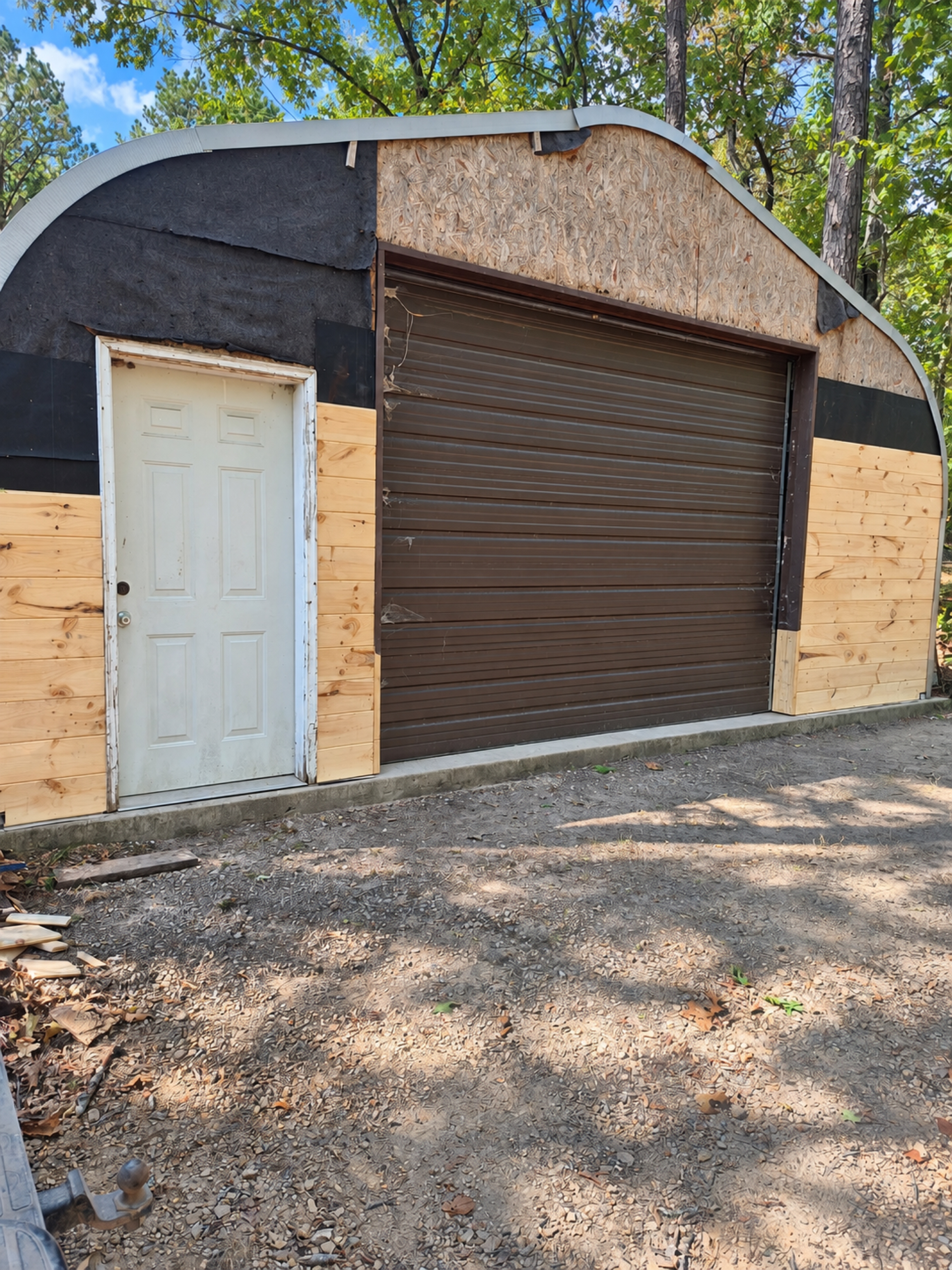 Garage front with new horizontal wood siding partly installed around the entry and overhead doors