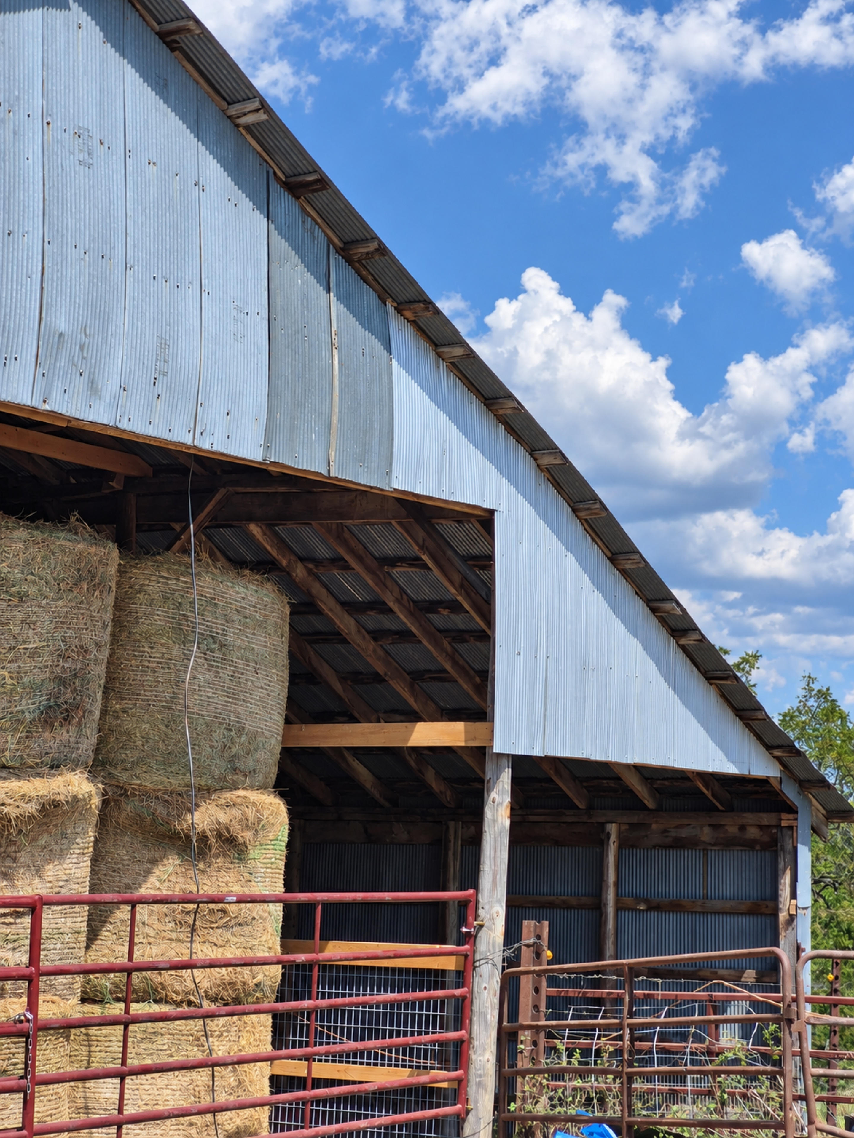 Angled front view of the barn’s corrugated metal facade, hay bays and red gates