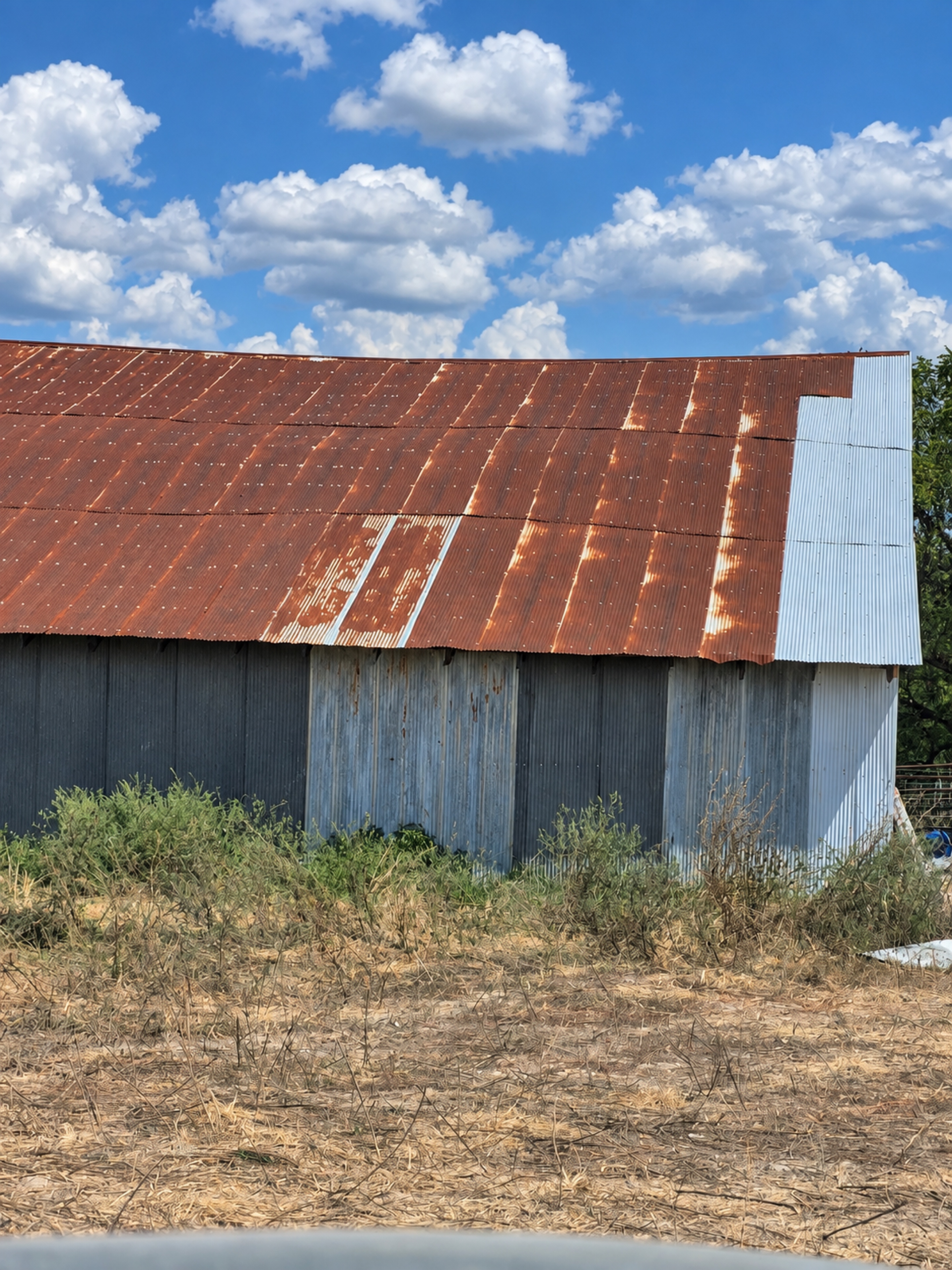 Weathered red barn roof with a section of silver corrugated replacement panels